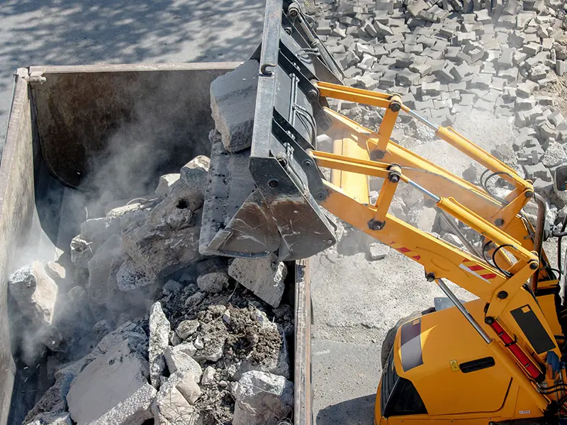 a tractor throwing large construction debris in a dumpster