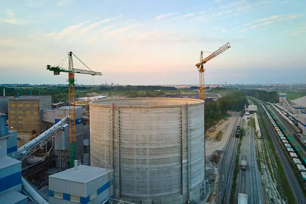 A-large-industrial-construction-site-featuring-a-massive-cylindrical-concrete-storage-tank-surrounded-by-cranes-and-factory-buildings